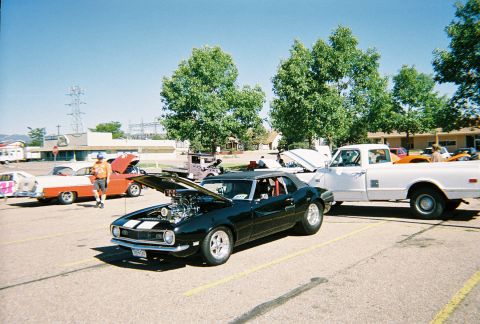 1972 Ford Ranchero - Several vehicles are parked in a lot under a clear blue sky, with trees and buildings in the background.