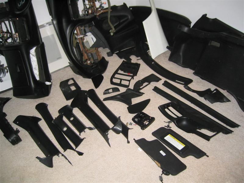 Disassembled black car interior trim parts spread on beige carpet