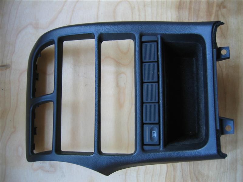 Black center console trim bezel with switch cutouts and defrost button on wood surface