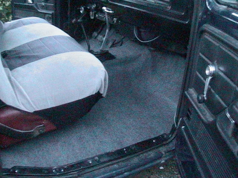 Truck cab interior with fresh gray carpet, covered bench seat, and open door showing window crank