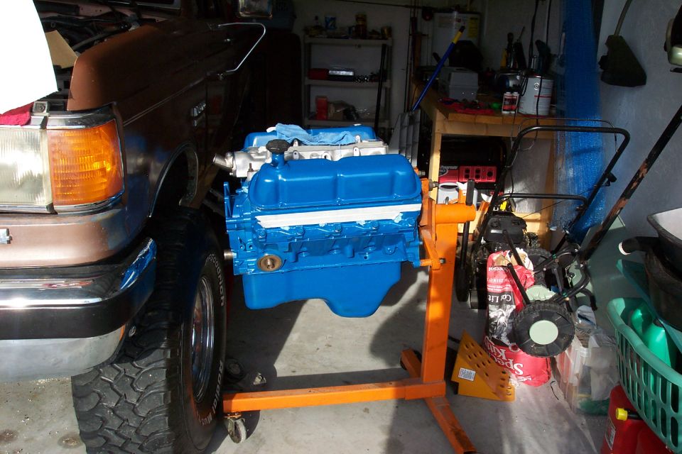 Blue engine on an orange stand next to a brown vehicle's front fender and tire