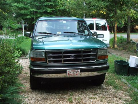 1996 Ford Bronco - A green Ford F-Series truck is parked in a gravel driveway, with a white van visible behind it.