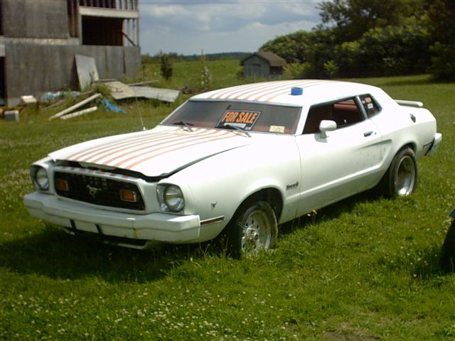 White 1978 Ford Mustang II coupe with racing stripes and a "FOR SALE" sign in the windshield