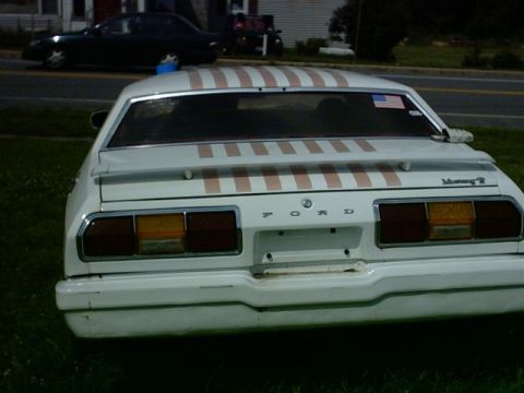 1978 Ford Mustang II - The rear of a white 1978 Ford Mustang II is shown with a striped decal on the trunk and an American flag sticker on the rear window.