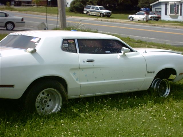 White coupe with custom wheels, stars on the side, parked on grass