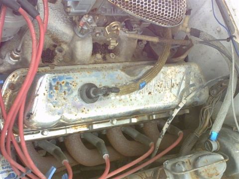1978 Ford Mustang II - Overhead engine-bay close-up of a V8's passenger-side chrome valve cover, pitted and spotted with rust, with a breather grommet in the cent…