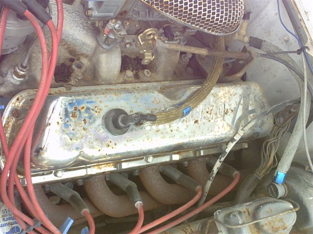 Rust-spotted chrome valve cover and cast-iron exhaust manifold with red plug wires