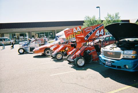 1972 Ford Ranchero - A collection of sprint cars and a GMC pickup truck are parked in a lot on a sunny day.