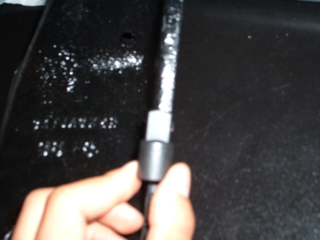 Black vehicle frame with embossed numbers and a hand holding a black cable with a gray connector