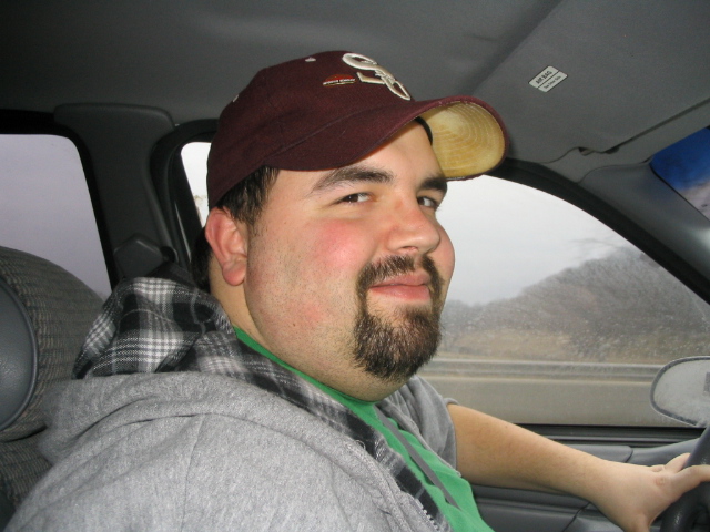 Man in maroon cap and gray hoodie sitting in driver's seat of a car