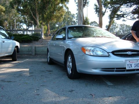1995 Ford Taurus - Silver sedan parked next to a white truck, showing its front 3/4 view with a California license plate.