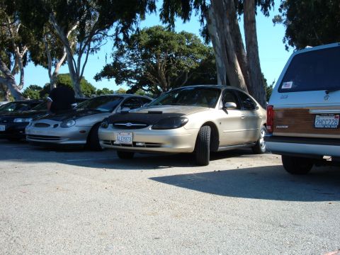 1995 Ford Taurus - Several cars are parked in a lot, including a 1995 Ford Taurus with a black car bra.