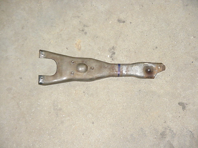 Metal clutch fork with a U-shaped end and a single mounting hole at the other end, resting on a concrete surface