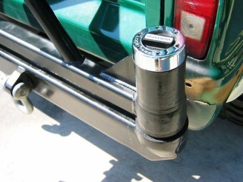 1995 Ford Bronco - A close-up of a custom fabricated rear swing-out tire carrier bolted to a green truck's rear bumper, pivoting on a chrome-capped WARN spind…