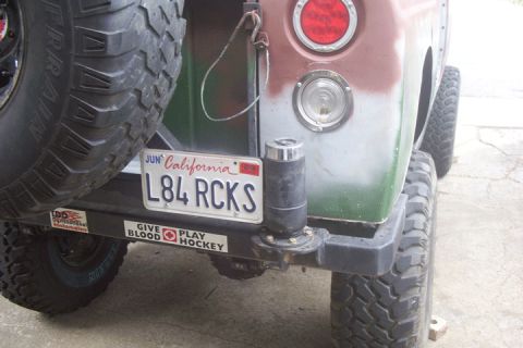 1995 Ford Bronco - Rear corner of a weathered green and gray off-road rig showing a California plate reading "L84 RCKS", a round red taillight and backup lamp…