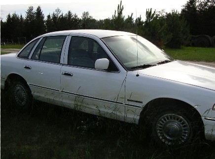 1998 Ford Crown Victoria - White 1998 Ford Crown Victoria sits in a grassy field with trees in the background.