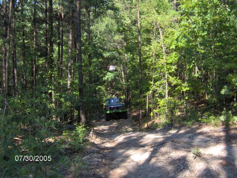 1978 Ford Bronco - An off-road SUV navigates a wooded trail, with another vehicle partially visible further up the path.