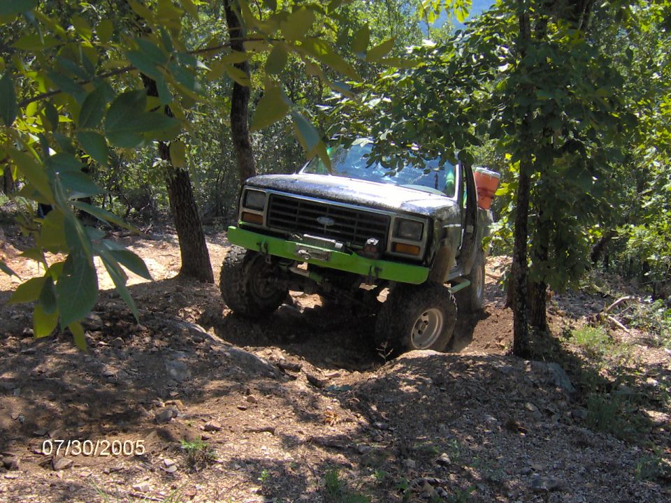Modified pickup truck with green bumper and winch navigating a dirt trail