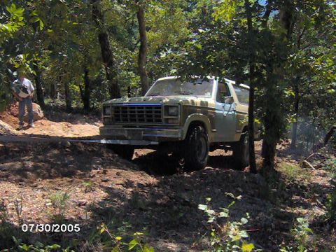 1978 Ford Bronco - A 1978 Ford Bronco navigates a wooded trail with a person standing nearby.