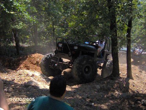 1978 Ford Bronco - A heavily modified Jeep navigates a challenging off-road course surrounded by trees.