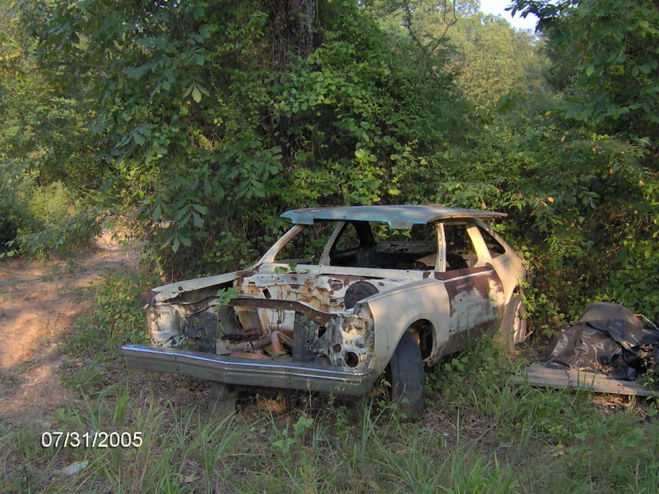 Abandoned 1978 Ford Pinto shell in woods, front end missing, rust visible