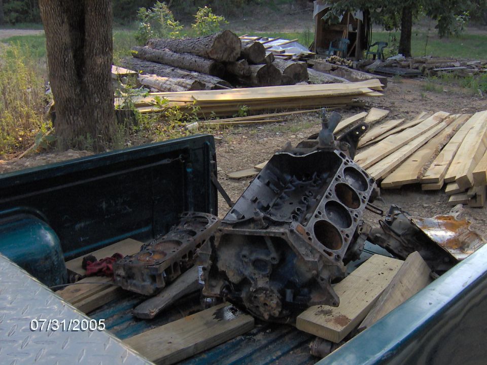 Greasy disassembled V8 engine block and cylinder head in a green pickup bed outdoors