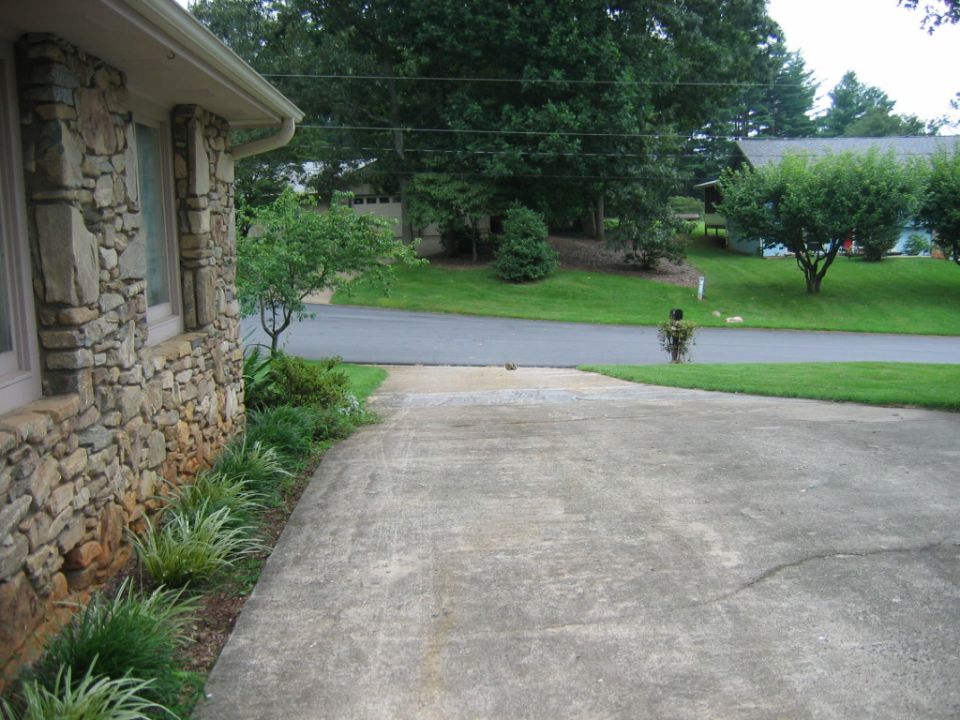 Driveway leading to a street with houses and trees in the background