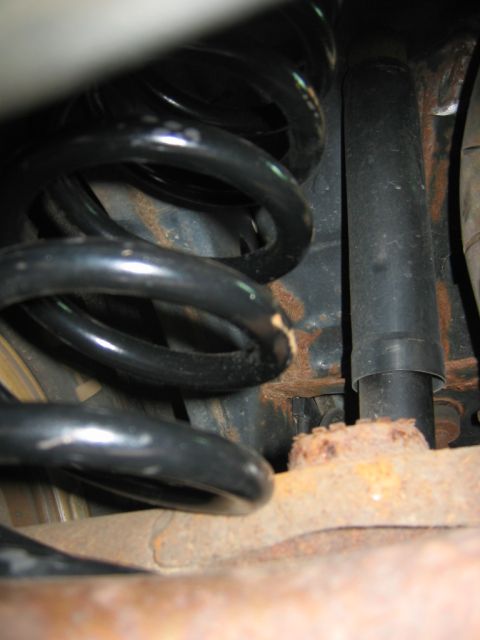 1985 Ford LTD Crown Victoria - Close-up view of a rusty rear suspension spring and shock absorber assembly.