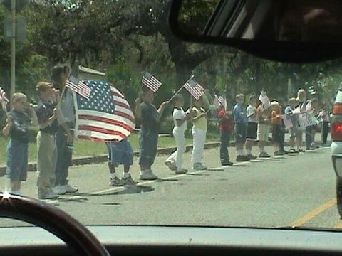 1987 Ford Bronco - A group of children stand in a line, each holding an American flag, participating in what appears to be a parade or ceremony.
