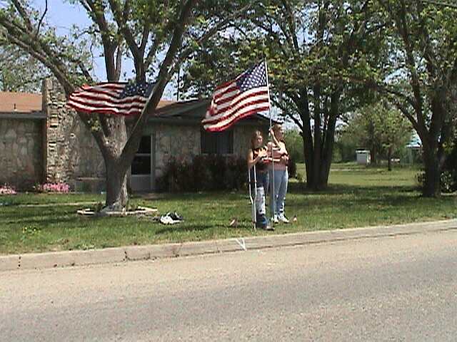 Two people stand with American flags in front of a house