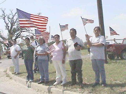1987 Ford Bronco - A group of people stand together holding American flags, with a red truck partially visible behind a fence.