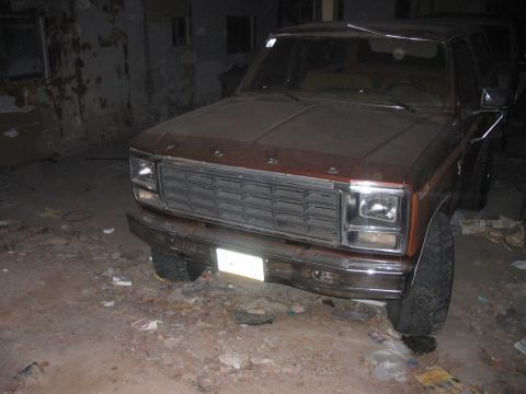 1986 Ford Bronco - A brown Ford Bronco is parked indoors, showing its front grille and headlights.