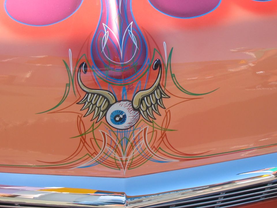 Car hood with orange paint, pinstriping, and a winged eyeball graphic
