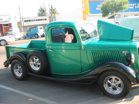 1986 Ford Bronco - A vintage green pickup truck is parked outside with its hood up, revealing a spare tire on its side.
