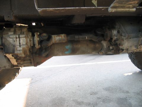 1986 Ford Bronco - A close-up view of a vehicle's drivetrain components, including the transfer case and driveshaft, with a blue marking on the housing.