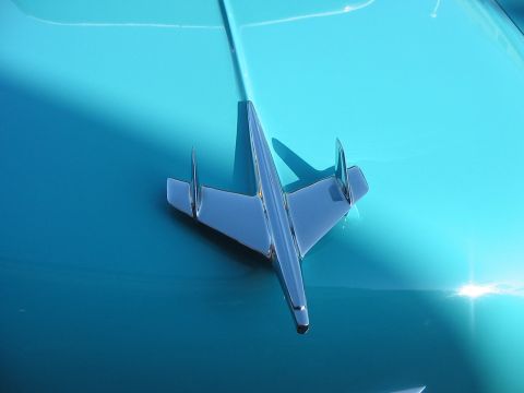 1986 Ford Bronco - A chrome airplane hood ornament is centered on the hood of a turquoise car.