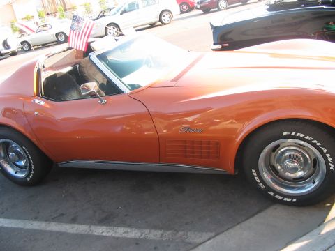 1986 Ford Bronco - An orange convertible sports car is parked next to other vehicles, with an American flag visible.