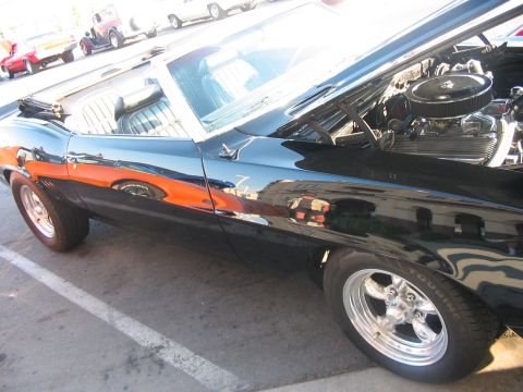 1986 Ford Bronco - A black convertible with its hood open, revealing the engine, sits in a parking lot with reflections of other vehicles on its side.