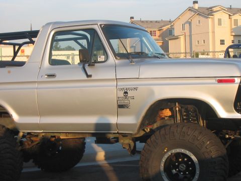 1986 Ford Bronco - This lifted SUV features large off-road tires, a roll cage, and custom decals on its side.