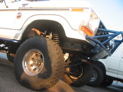 1986 Ford Bronco - A modified white Ford Bronco sits low to the ground, showing off its large tires and custom front bumper.