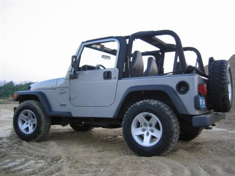 2000 Jeep Wrangler - This Jeep Wrangler is shown from a 3/4 rear angle, parked on a dirt surface with a clear sky above.