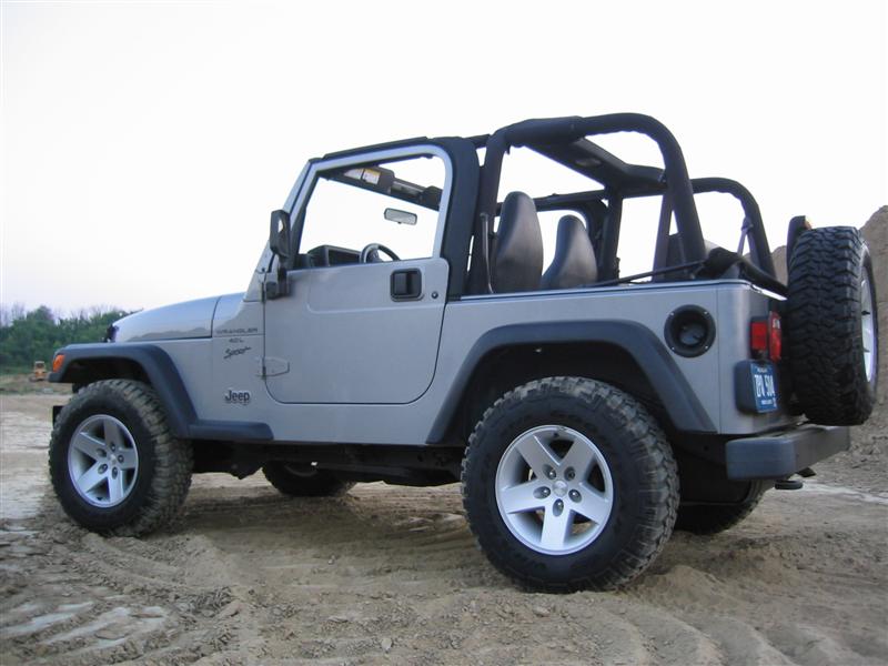 Silver Jeep Wrangler, rear quarter view, parked on dirt. Has a spare tire on the back