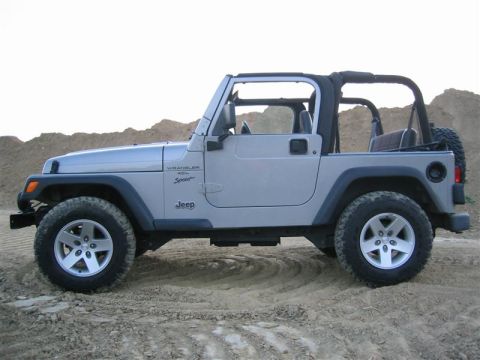 2000 Jeep Wrangler - A silver 2000 Jeep Wrangler Sport 4x4 is shown from the side, parked on a dirt surface with a pile of dirt in the background.