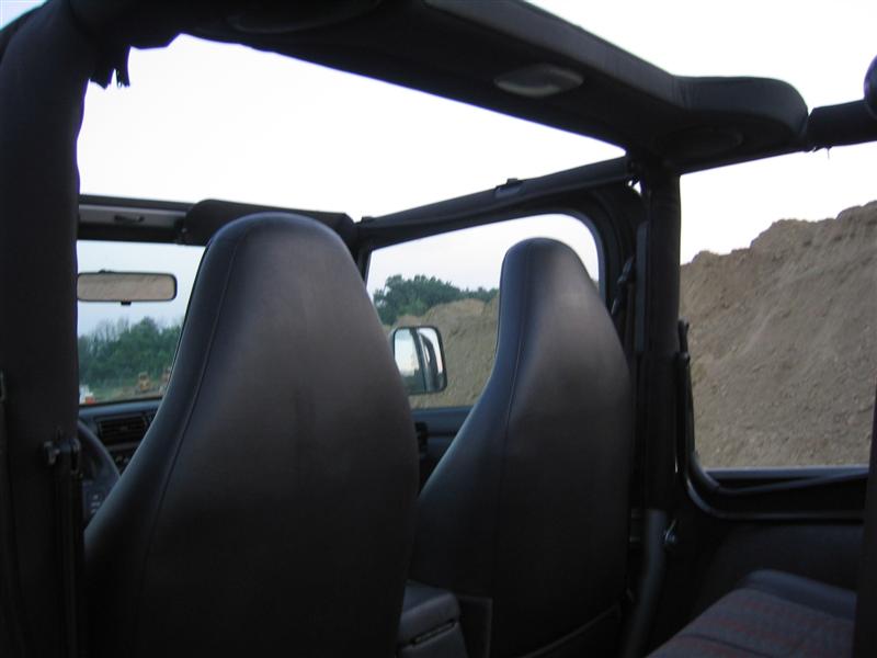 Rear-seat view of topless Jeep Wrangler interior with roll bar and front seats