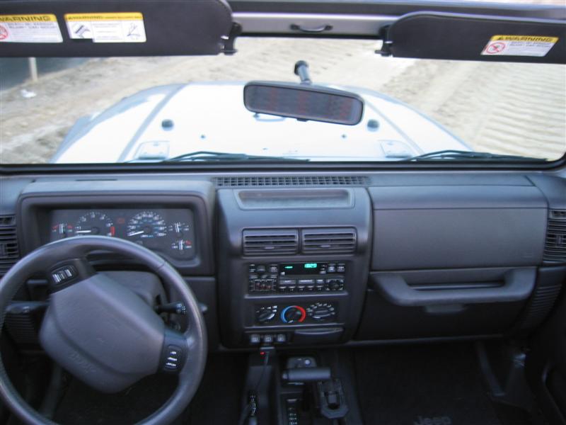 Jeep Wrangler TJ interior from driver's seat showing gray dash, gauges, radio and white hood beyond windshield