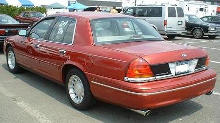 1999 Ford Crown Victoria - Rear view of a red sedan parked in a lot with other vehicles.
