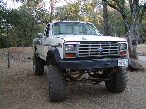 White Ford pickup truck with large tires and lifted suspension, parked outdoors