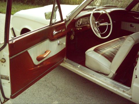 1962 Ford Falcon - The interior of a 1962 Ford Falcon features a white steering wheel and two-tone red and white seats and door panels.