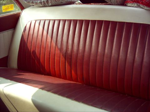 1962 Ford Falcon - The interior of a classic car features a red and white bench seat with decorative pillows.