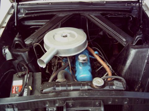 1962 Ford Falcon - The engine bay of a 1962 Ford Falcon shows its blue engine block and silver air cleaner assembly.